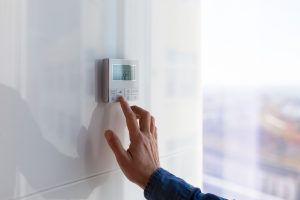 Une main appuyant sur le thermostat d'une maison